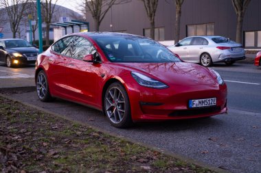 modern kırmızı elektrikli Tesla Model 3 caddede, kentsel çevrede çevre dostu elektrikli araç, otomotiv endüstrisi, sürdürülebilir ulaşım, Frankfurt, Almanya - 19 Şubat 2024