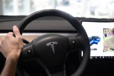 erkek sürücü kolunda, direksiyon başında Tesla modeli Y model elektrikli araba, modern yolcu vagonu, gösterişli iç mekan kontrol tekerleği, vites kolları, ön cam ve ön panel