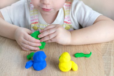 Küçük bir çocuğun, sarışın bir kızın ellerinde plastik oyuncaklar. 2 yaşında heykeller, renkli hamurdan karakterlerin figürleri. Güzel motor beceriler kavramı, dokunsal hisler, yaratıcılık.