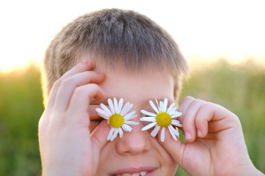 Çocuk, mutlu romantik çocuk elinde papatya çiçeğini gözünün önünde tutuyor, yeşil güneşli çayır yüreğinde, mutlu çocukluk, doğal dünya, yaz dönümü kutlamaları