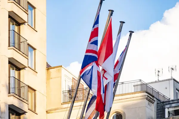 stock image Flags United Kingdom and Canada flutter against backdrop building facades, international friendship and shared heritage, representing unity and cooperation, blowing in wind, national pride