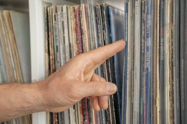 tutkulu yaşlı bir adam, nostaljiye dalmış, sevgiyle diski seçiyor, rafta vinil albüm, altın çağ müziği ve geçmiş ile bağlantı kuruyor, Frankfurt - 29 Mayıs 2024