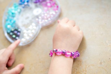 Kızın elleri bilezik yakın plan, sanat ve zanaat aktivitesi, DIY el işi, renkli boncuklarla kişiselleştirilmiş bilezik, güzel motor beceriler.