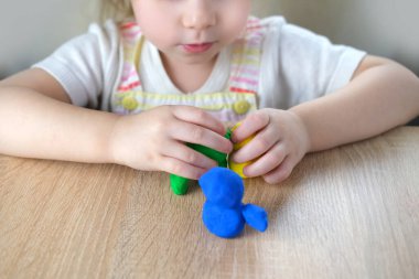 Küçük bir çocuğun, sarışın bir kızın ellerinde plastik oyuncaklar. 2 yaşında heykeller, renkli hamurdan karakterlerin figürleri. Güzel motor beceriler kavramı, dokunsal hisler, yaratıcılık.