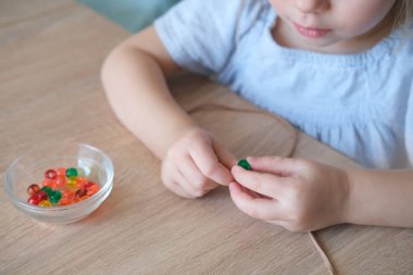Küçük çocuk, sicimin üzerine renkli plastik boncuklar dizen bebek, çocuğun parmakları yakın plan, iyi motor becerilerin gelişimi konsepti, dokunsal hisler, yaratıcılık, çocuk eğlencesi