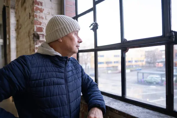 stock image mature sad man, senior 60 years thoughtfully at panoramic window, emotional distress and life challenges, anxious anticipation, emotional turmoil, life difficulties, inner turmoil