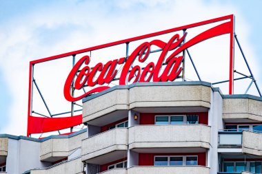 Popüler kültür ikonu Coca-Cola logosu yüksek katlı binanın tepesinde içecek markasının küresel erişimini sergiliyor, ferahlatıyor ve eğlendiriyor, Berlin, Almanya - 24 Nisan 2024