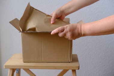 Kadınların ellerinin yakın çekimi, açık karton posta kutusundan paketleri paket kağıdı, paket, sipariş edilmiş malların teslimatı, çevrimiçi alışveriş, müşterilere zamanında teslim edilmesi.