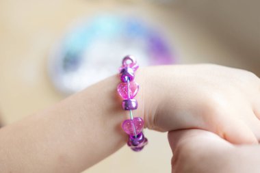 Kızın elleri bilezik yakın plan, sanat ve zanaat aktivitesi, DIY el işi, renkli boncuklarla kişiselleştirilmiş bilezik, güzel motor beceriler.