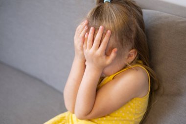 Küçük çocuk 5 yaşında, sarışın kız ağlıyor, yüzünü örtüyor, erken teşhis ve müdahale, otistik insanlara destek, koruyucu duruş, aile içi şiddetten şikayetçi.