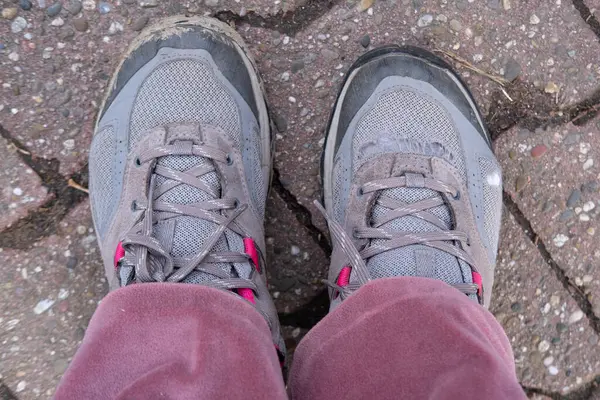 Stock image old worn-out shoes, hiking boots on female foot on floor, signs of wear and tear, adding to character, Poverty and Homelessness, Many miles walked on worn-out sneakers