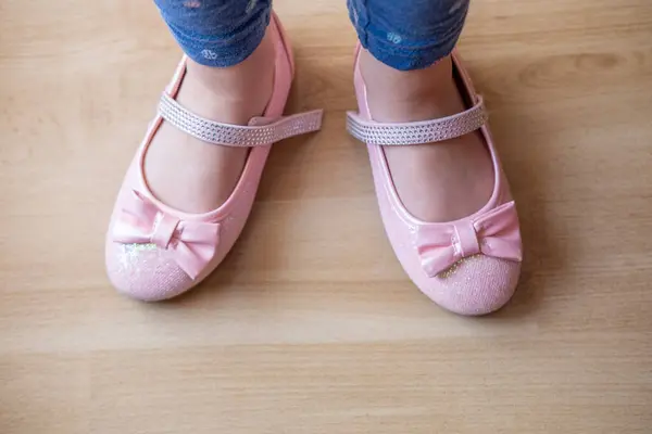 stock image child, 5-year-old girl in shiny pink shoes with bows, worn incorrectly, confusing left and right shoes, Nurturing self-reliance, learn and grow