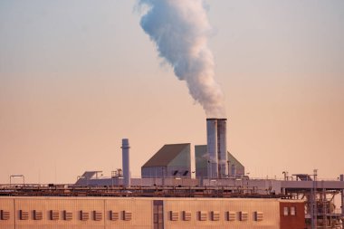 Bacadan çıkan buharlı dramatik manzara fabrikası, gün batımına doğru yükseliyor, gücü ve endüstriyi yakalıyor, sanayileşmenin çevresel etkisi, modern dünyanın sürdürülebilir uygulamaları,