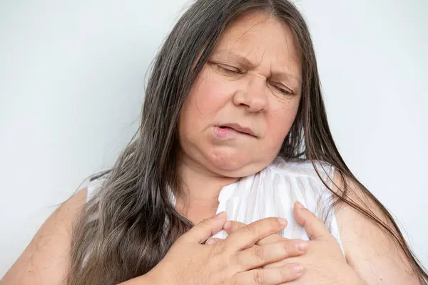 stock image diseased mature woman holds to heart, experiences sudden chest pain, Arterial hypertension, Myocarditis or Arrhythmia, Ischemic heart disease, seeking immediate medical attention