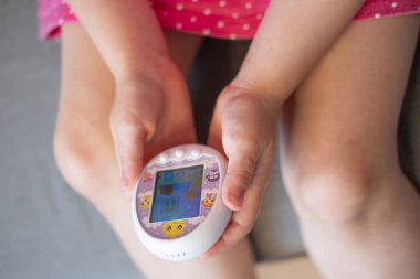 çocuk eli nazikçe Tamagotchi oyuncağı, popüler sanal hayvan çılgınlığı için nostalji çağrıştırıyor 1990 'larda empati geliştirme, çocukluk anılarını besleme, Frankfurt - 10 Şubat 2024