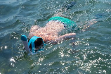 Genç çocuk deniz suyunda şnorkelle yüzmekten hoşlanıyor, aktif yaz tatillerinin tadını çıkarıyor, maske ve şnorkelle sualtı yaşamını keşfediyor, su aktiviteleri, çocukluk macerası, deniz hayatını merak ediyor.