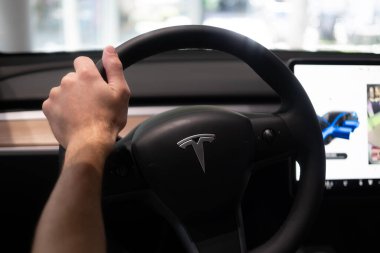 erkek sürücü kolunda, direksiyon başında Tesla modeli Y model elektrikli araba, modern yolcu vagonu, gösterişli iç mekan kontrol tekerleği, vites kolları, ön cam ve ön panel