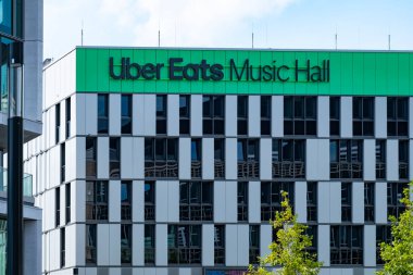 Uber Eats Music Hall Advertising logo on modern building facade, fusion of food tech and music in bustling urban setting, Berlin, Germany - August 16, 2024 clipart