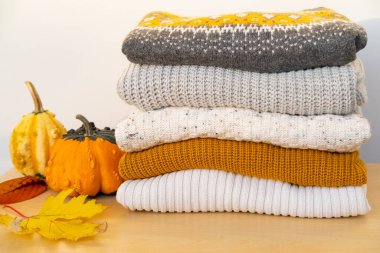 Sonbahar renklerinde yumuşak, örülmüş kazak yığını balkabakları ve yaprakların yanında sergilenerek sıcak ve davetkar bir atmosfer yaratıyor.