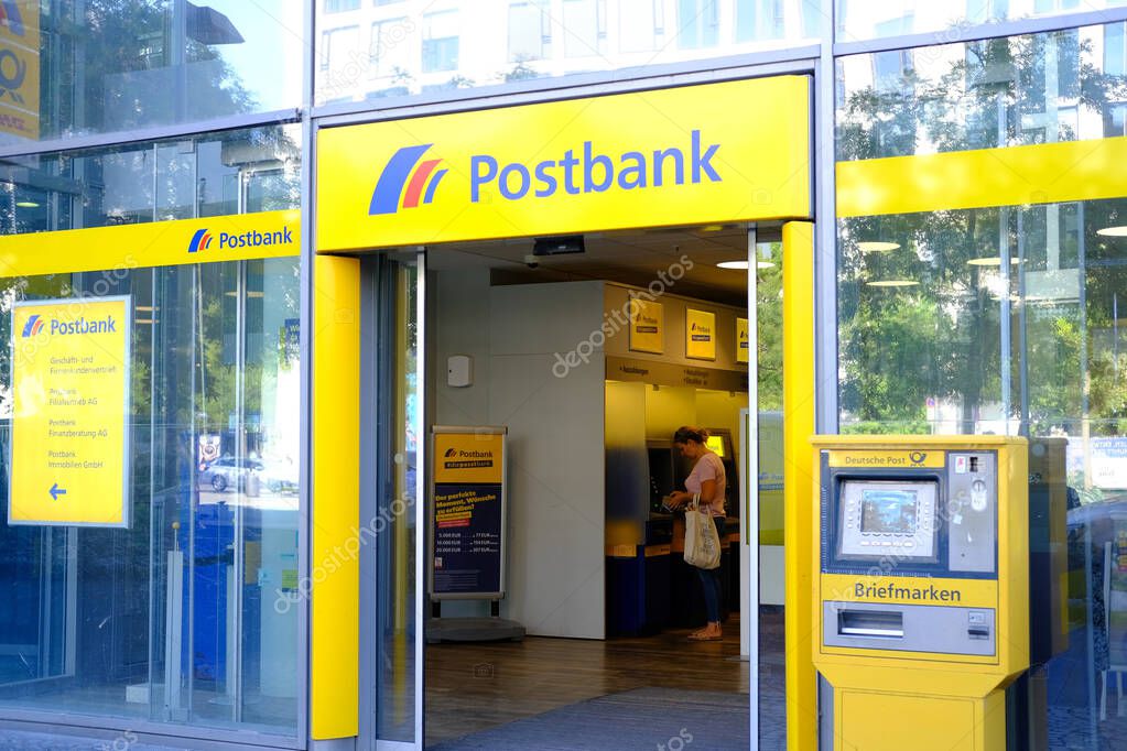 Bright yellow facade European bank Postbank branch invites customers inside, customer interacts with ATM modern bank branch in Germany, Frankfurt - May 28, 2024