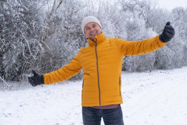 Parlak sarı ceketli mutlu yaşlı adam sakin karla kaplı manzaralarla, kış yürüyüşleriyle, sağlıklı yaşam tarzıyla, soğuk havayla çevrili güzel parklarda rahatça geziniyor.