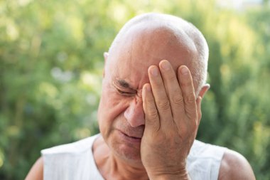 65 yaşındaki yaşlı adam kederden ağlıyor, şiddetli baş ağrısı yaşıyor, başını tutuyor, sakız iltihabı, yaşlılıkta sağlık.