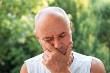 65 yaşındaki yaşlı adam kederden ağlıyor, şiddetli baş ağrısı yaşıyor, başını tutuyor, sakız iltihabı, yaşlılıkta sağlık.