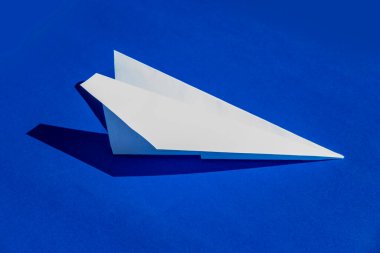 Beyaz kağıt uçak uçar, sembol umut ve mavi arka plana karşı yeni başlangıçlar yapar, DIY origami kağıt uçak rüyaları ve özünde uçuşu ve özlemleri simgeler.