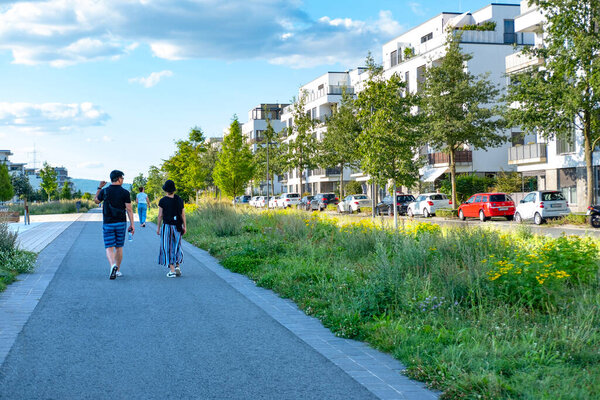 люди ходят по жилым зданиям с пышной зеленью, современной архитектурой и ухоженным ландшафтом, новые многоквартирные дома, Франкфурт - 25 августа 2024