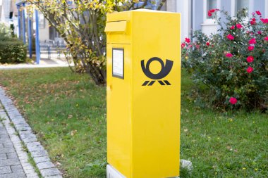 Alman Sarı Deutsche Posta Kutusu, çiçekler ve yeşilliklerle park halinde duruyor, Almanya, Frankfurt 'ta posta hizmetlerini sembolize ediyor - 28 Mayıs 2024