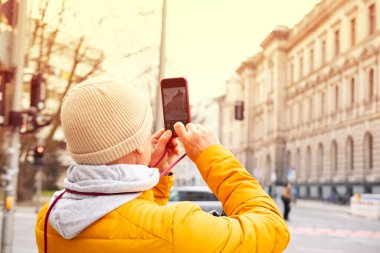 man tourist explores Berlin with phone, wearing vibrant orange jacket and enjoying city's atmosphere, Traveler captures Berlin's essence, leisurely walk through clipart