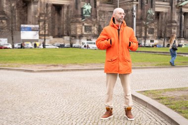 Turist, canlı turuncu ceketiyle Berlin 'i keşfeder ve şehrin atmosferinden zevk alır. Gezgin, Berlin' in özünü yakalar ve rahatça yürür.