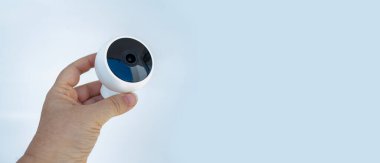 Beyaz arka plan, modern ev gözetlemesi ya da akıllı ev ayarlarına karşı gösterişli tasarımı olan küresel, küçük güvenlik kamerası tutan kişi
