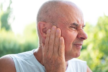 60-65 yaşlarında mutsuz yaşlı bir adam, kulak ağrısı, kulak ağrısı, ekşitme, sağlık sorunları, Tinnitus semptomları, keskin ağrı kesici arayışı içinde.
