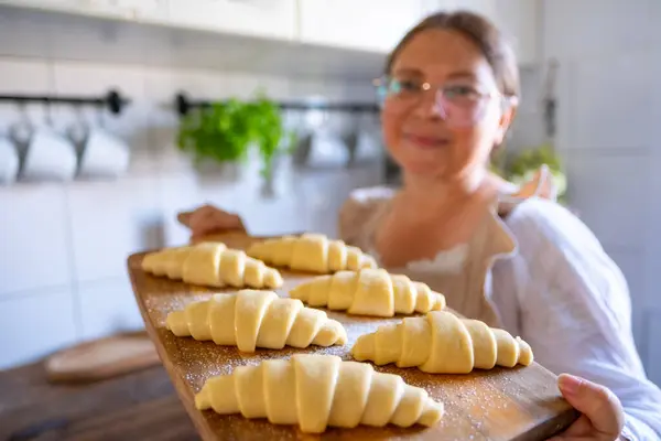 stock image woman in vintage dress, apron preparing croissants, Unbaked, flaky croissants on wooden board, prepared for oven, homemade pastry in kitchen interior