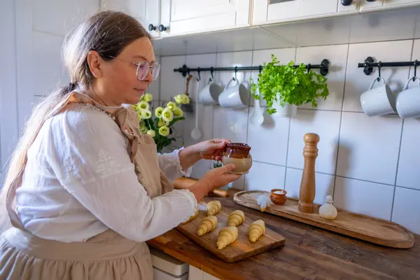 stock image woman housewife, housekeeper, wife in linen old-fashioned apron prepares croissants, traditional retro kitchen interior, Unbaked raw homemade flaky croissants