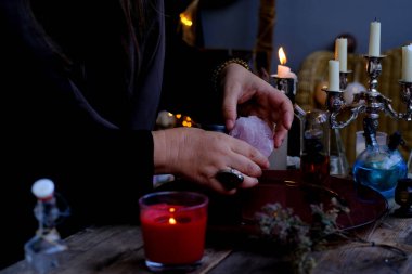 healing session in the salon of healer, herbalist, close-up of hands of female psychic hold rose quartz stone, burning candles, dried herbs, concept of alternative medicine, esoteric practices