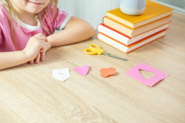 Anaokulu öğrencisi kız makas becerilerini renkli kağıtlardan ev, kalp ve çiçek gibi şekilleri keserek geliştiriyor.