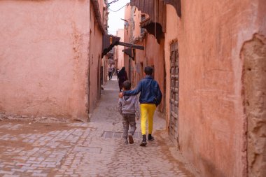 İki kardeş caddede yürüyor, büyük kardeş sevgiyle genç olanı kucaklıyor, arkadan bakıyor, aile sevgisi, otantik Afrika manzarası, günlük aktiviteler
