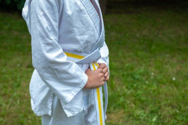 Genç judocu çocuk, judo üniformalı çocuk beyaz-sarı kuşak bağlayan, dövüş sanatlarında kendini adamış ve güçlü, dövüş sanatları eğitimi, fiziksel fitness, atletik beceriler