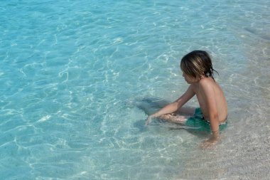 Çakıl taşlı sahilde hafif dalgaların tadını çıkaran çocuk, doğal güzellik kıyılarıyla çevrili, deniz ile huzurlu bir an, su maceraları çocuklarda merak ve çevreye olan sevgiyi artırıyor.