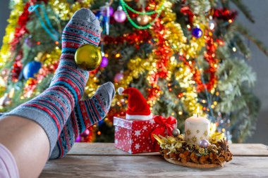 Sıcak kış sahnesi, renkli Noel çorapları giyerek, Noel ağacının yanında dinlenerek, rahat kış sahnesi, sıcak ve davetkar atmosfer, tatil ruhu.