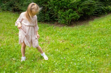 Sarışın 5 yaşındaki zarif elbiseli kız çayırdaki yeşil çimlerde, konsept mutluluk çocukluğu, geleneksel aktivite