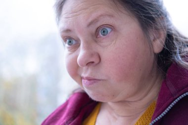 Stresli 50 yaşında bir kadın, çevresi yeşillik ve dingin çevre ile çevrili, negatif duygular sergiliyor, öfke ve gerilimle tepki veriyor, duygusal dengesizlik gösteriyor.