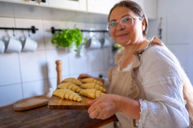 Klasik elbiseli bir kadın, kruvasan hazırlayan bir önlük ahşap tahtanın üzerinde pişmemiş, pullu kruvasanlar fırın için hazırlanmış, mutfak içinde ev yapımı hamur işi.