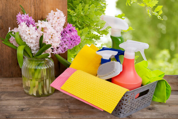 Корзина с чистящими средствами на размытом весеннем фоне, салфетки, моющие средства, гиацинтовые цветы в вазе на столе, весенняя уборка дома, свежесть и жизнеспособность, организация и разборка дома