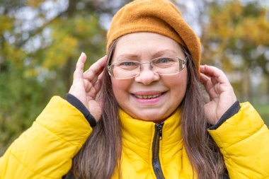 Neşeli, olgun bir kadın eğleniyor, komik bir yüz ifadesi yapıyor, neşeli hareketlerle komik bir resim yapıyor, garip bir ifade sergiliyor, açık havada kendiliğinden çekilen bir an.