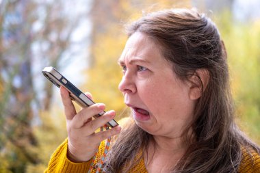 Orta yaşlı, gergin, saçları dalgalı bir kadın. Sinirli bir şekilde telefonda, stresli ve kontrolsüz duygularla bağırıyor. Öfkeli bir ifade, duygusal bir mücadele.