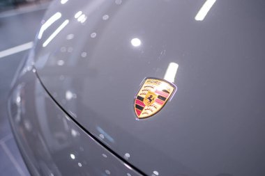 İkonik Porsche arması, otomobil galerisindeki gri Porsche Macan, gelişmiş otomotiv teknolojisi, Alman mühendisliği, yüksek teknoloji, kaliteli araç, Frankfurt - 25 Ocak 2025