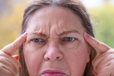 Olgun kadın yüzü kadın 50-55 yaşlarında görünüyor, göz çevresindeki kırışıklıkları inceliyor, göz kenarındaki jestleri, zihinsel yorgunluğu, yaşla ilgili değişiklikleri, hafıza kaybı, estetik bakım, yaşlanma önleyici prosedürleri